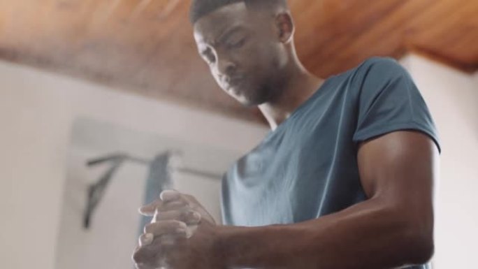 年轻的成年黑人男性在室内健身馆进行举重运动时，手上擦粉。