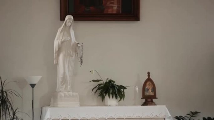 手里拿着念珠的白色圣母玛利亚雕像站在白色基座上