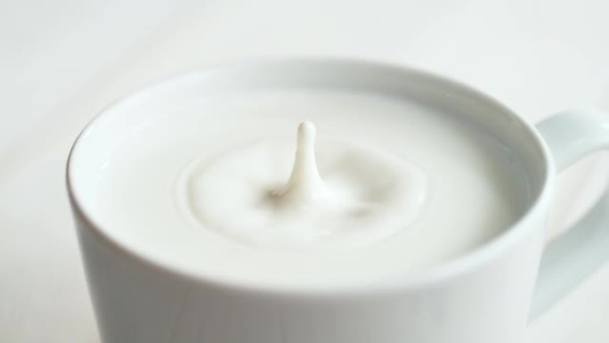 牛奶滴落入明亮背景下的奶油色液体的杯子