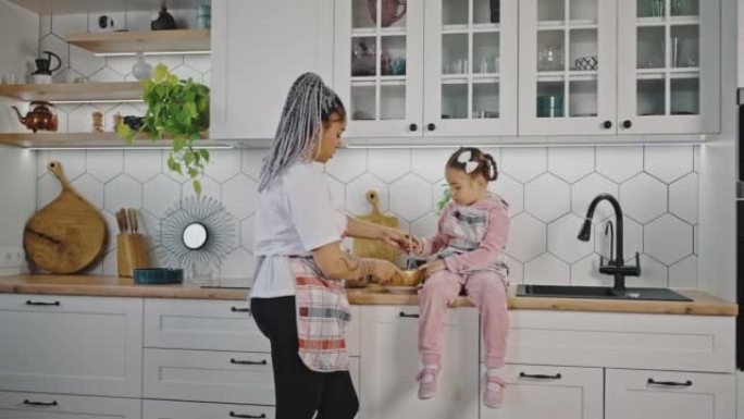 家庭烹饪。可爱的非洲裔美国母亲教她的小女孩在厨房里和打蛋器一起煮面团