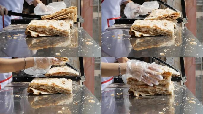 面包师的手用特制的断头台刀切开了许多层亚美尼亚拉瓦，并将其堆叠在闪亮的金属桌子上。慢动作
