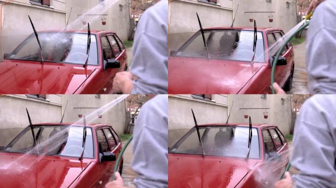 一名高级男子手里拿着软管，在后院洗车。