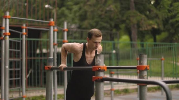 Fit man doing triceps dips on parallel bars at par