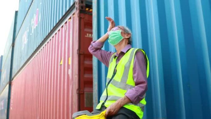 疲惫的亚洲高级男性集装箱工人戴着防护面罩、安全帽和制服。人牵手疼痛发炎，手腕肌腱炎。