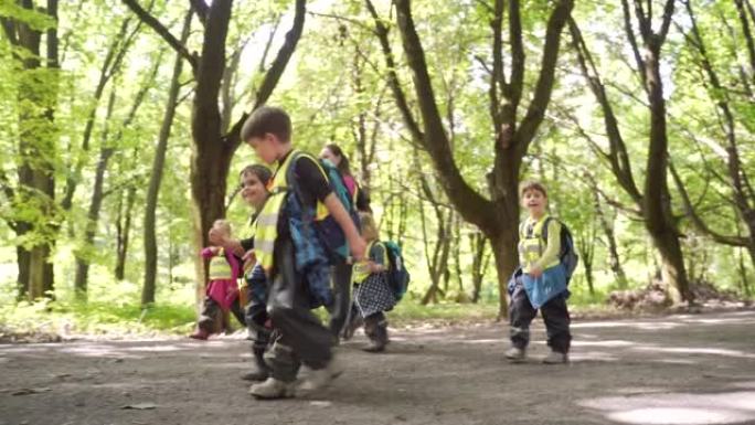 一群小孩沿着胡同公园幼儿园徒步旅行。孩子们在夏季森林营地散步。学前班，背包穿着冒险之旅林地。户外木学