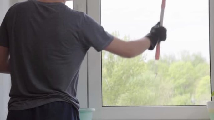 男人用特殊的泡沫清洗窗户并清洗它们。清洁服务。穿着黑色手套清洁窗户的工人，家里有抹布、刮刀和清洁剂喷