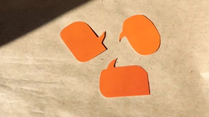 4k视频，从橙色纸上切出的三个语音气泡的特写镜头，并留有文字空间。在棕色牛皮纸上旋转，俯视图。DIY