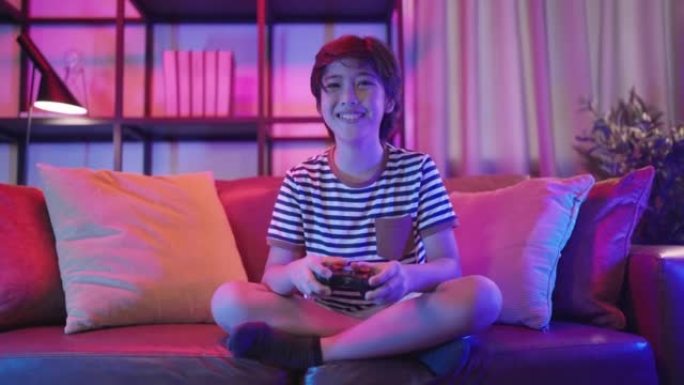 退出微笑开朗的亚洲少年男孩在家里的客厅沙发上玩手机游戏智能手机应用程序，亚洲儿童男性坐在沙发上使用智
