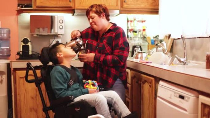 拉丁美洲母亲在家庭厨房内照顾轮椅上的残疾儿子