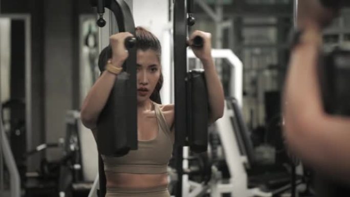美丽的亚洲健身女性坐在胸蝇机上锻炼。