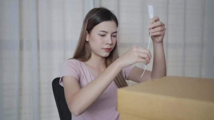 女人的手正在用剪刀剪掉锁住棕色纸板箱的白色塑料封条。