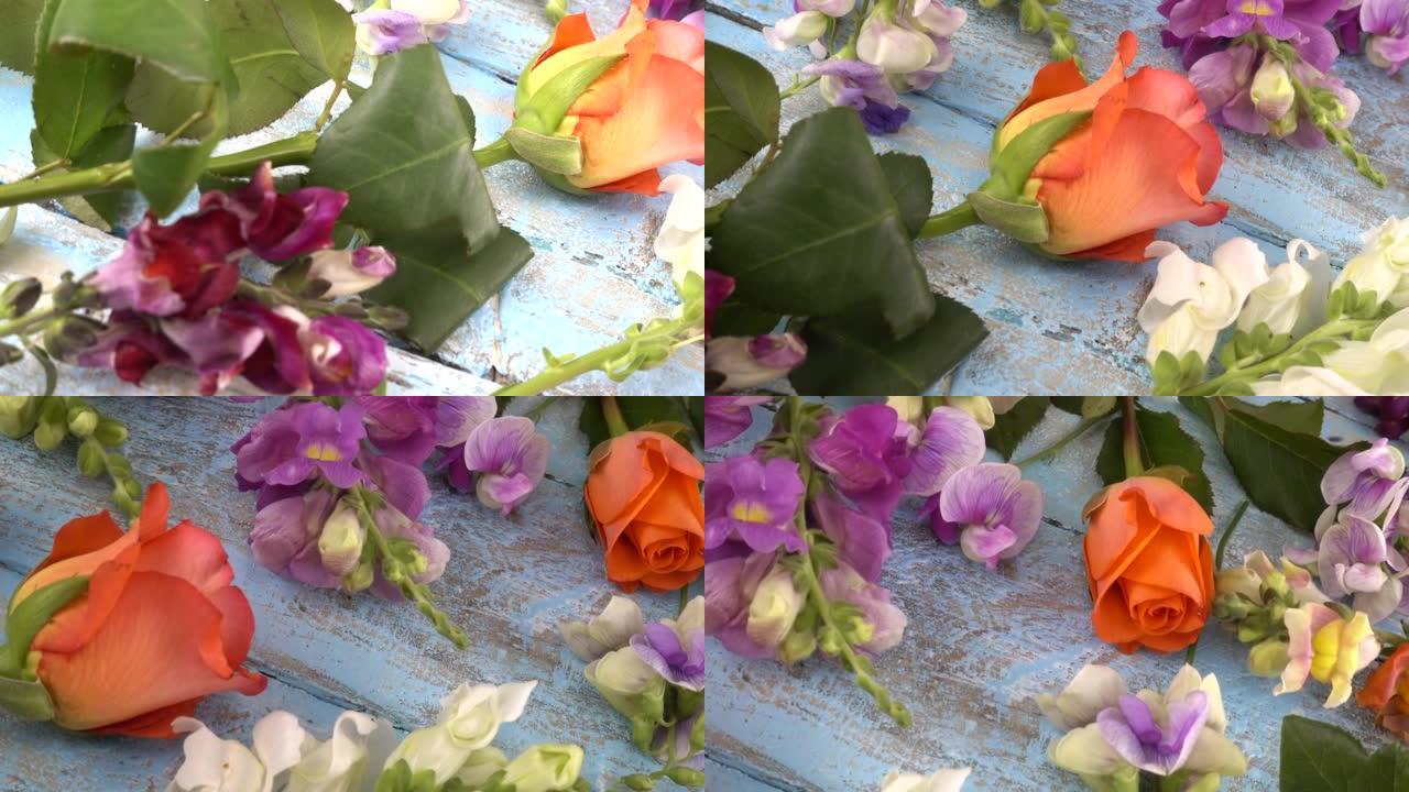 五颜六色的夏季花园花卉: 龙花、玫瑰、甜豌豆在复古木质浅蓝色背景上。