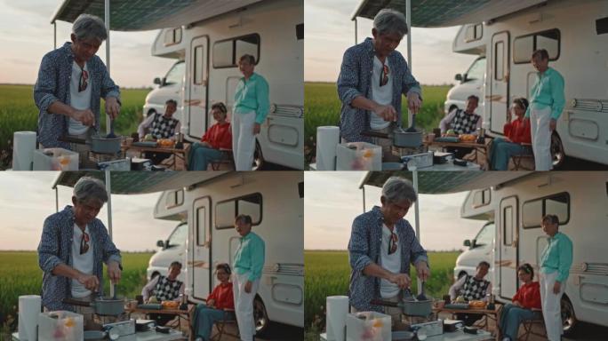 亚洲华人老人在周末休闲活动中为停在稻田的露营车旁边的高级朋友做饭