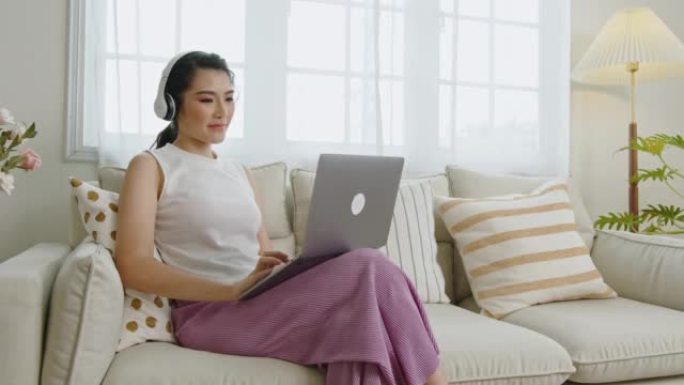 微笑的年轻亚洲女商人在家里的沙发上放松时使用笔记本电脑。在家工作的概念。