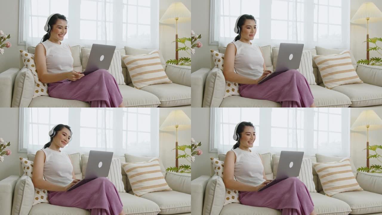 微笑的年轻亚洲女商人在家里的沙发上放松时使用笔记本电脑。在家工作的概念。