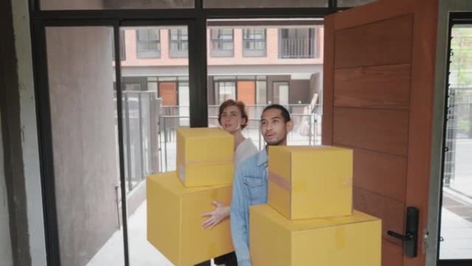 快乐的亚洲夫妇拿着堆叠的纸箱，在搬家的日子里穿过木门走进新房子。幸福家庭在大房子里四处寻找，购买房地