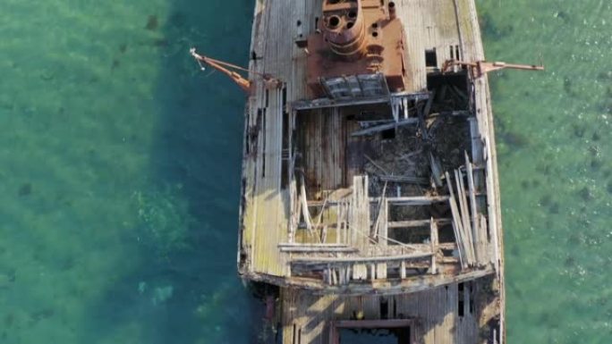 一艘失事的木船躺在海边，上面布满了铁锈。无人机视图