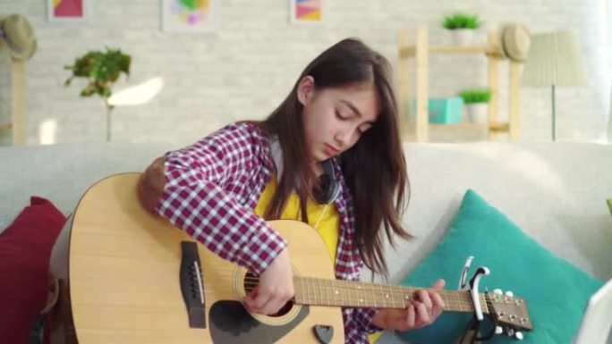 现代家居客厅长发美丽的亚洲女孩肖像原声吉他观看笔记本电脑在线训练特写