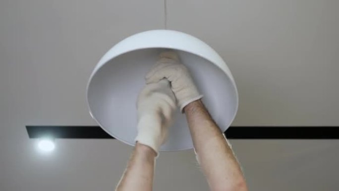 电工打开吊灯上的灯。更换公寓中烧坏的灯泡，主人将灯泡拧成现代吊灯