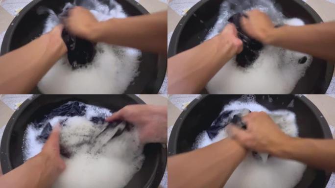 在第一人称视角中，男人的手在塑料盆里洗一件脏衬衫。
