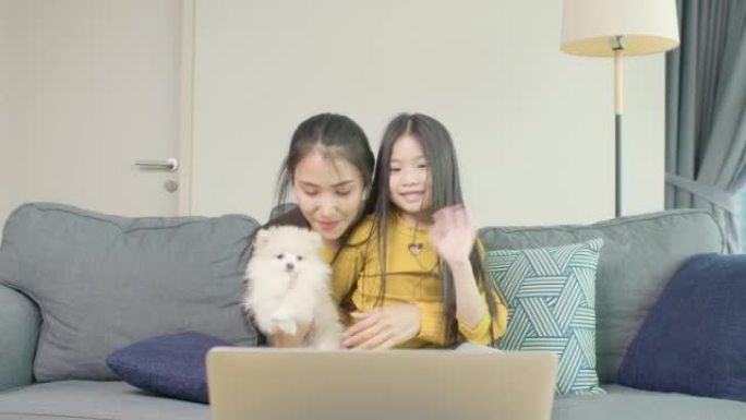 母女和他们的小狗在家里通过笔记本电脑进行视频通话打招呼
