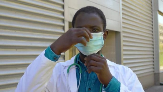 年轻的黑人医生戴着面具盯着相机保护，病毒
