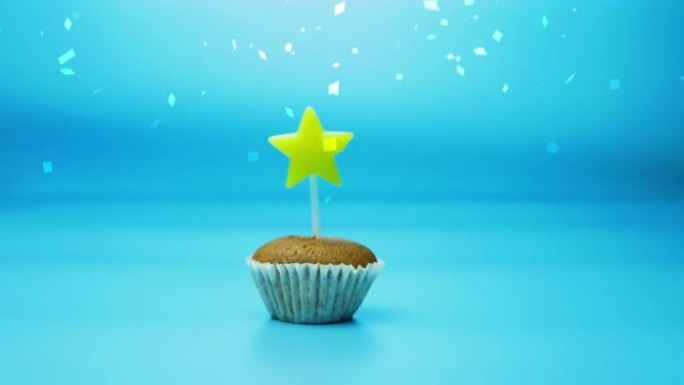 节日烘焙纸杯蛋糕，蓝色背景上有一支燃烧的星星形状的蜡烛。生日快乐或其他节日背景