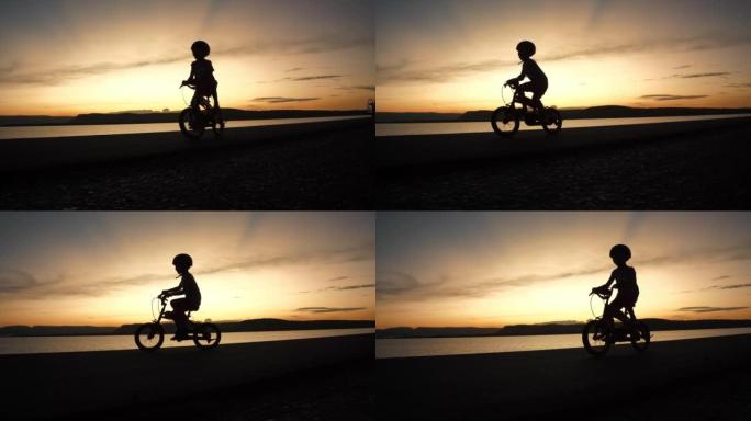 快乐的小男孩在日落时骑自行车。