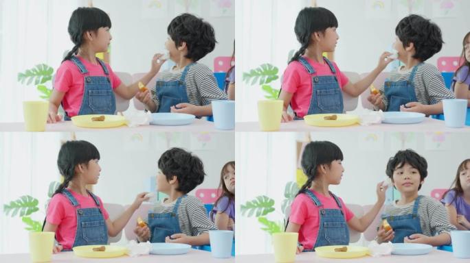 两个亚洲小孩学生一起在桌子上吃午饭。可爱的小学龄前女孩和男孩在幼儿园托儿所的教室里休息时感到快乐和喜