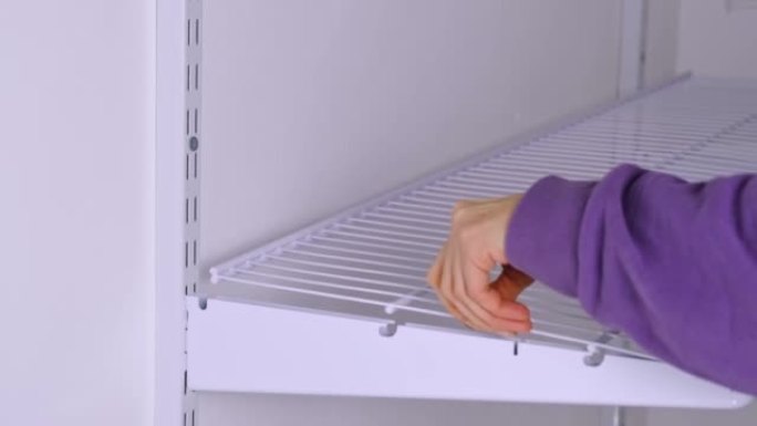 将金属网架安装在更衣室系统中的支架上。一个穿着紫色连帽衫的女人正在组装一个白色存储系统