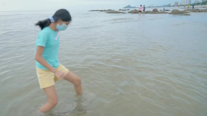 亚洲女孩戴着口罩在冲浪前在海滩上放松，生活方式理念。