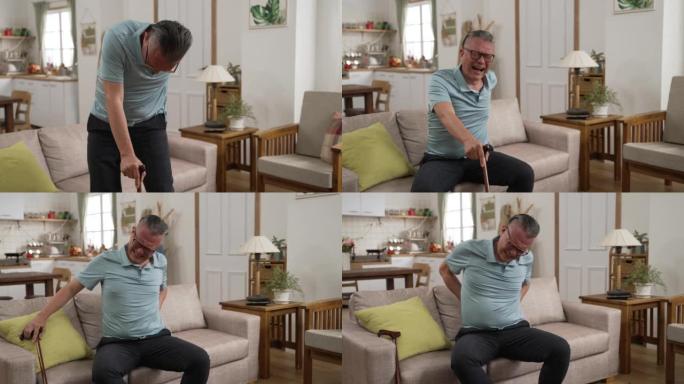 亚洲受伤的老年女性背部疼痛的慢动作正拄着拐杖慢慢走到沙发上，坐下休息。