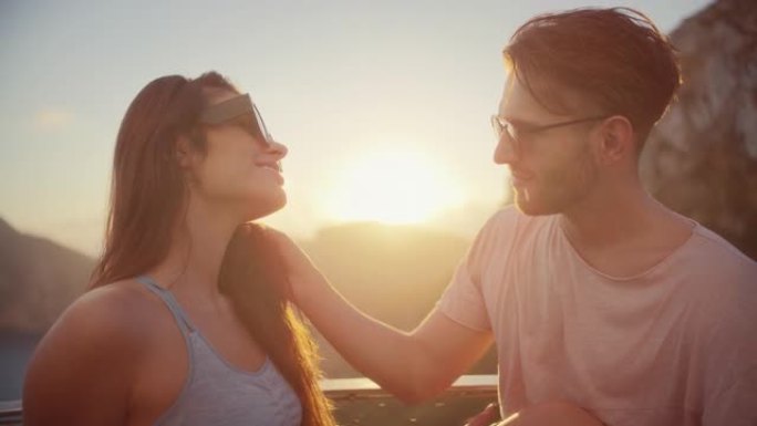 浪漫的夏天。夫妇在度假时戴着墨镜坐在长凳上，背景是金色的日落。热情的吻