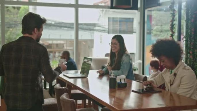 年轻人在咖啡馆柜台拿快递。客户在当地的小型企业拿起咖啡，然后与朋友坐在餐桌旁。咖啡店商务室内。