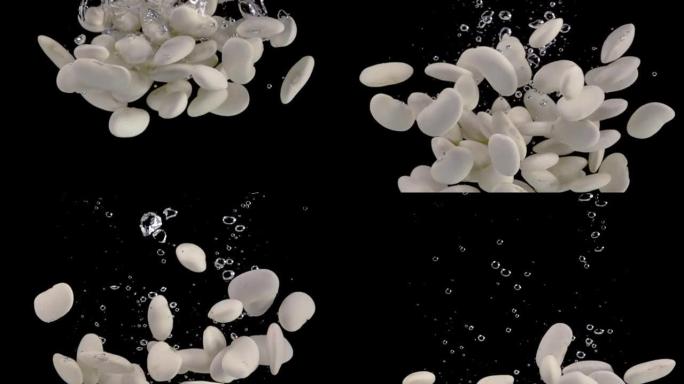 超级慢动作，一堆白芸豆落到水中，黑色背景上有气泡。以1000 fps的速度在高速电影摄像机上拍摄。S