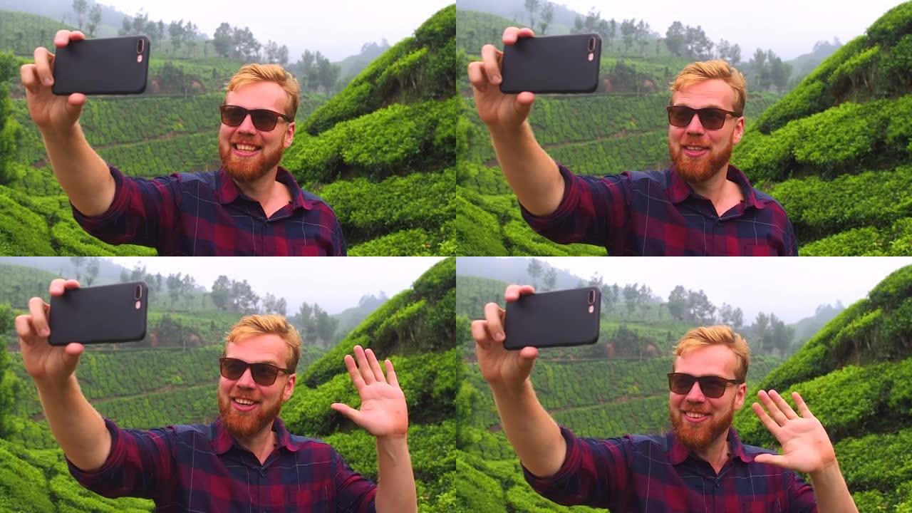 戴着墨镜的红发姜大胡子男人通过智能手机视频聊天，向印度munnar kerala茶园问好