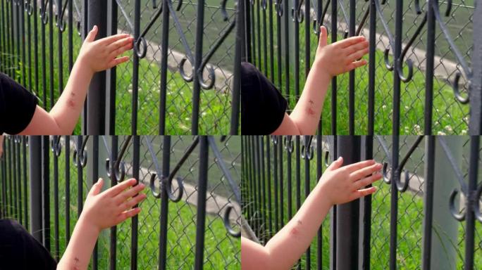 忧郁的年轻白人女孩触摸金属栅栏与手指