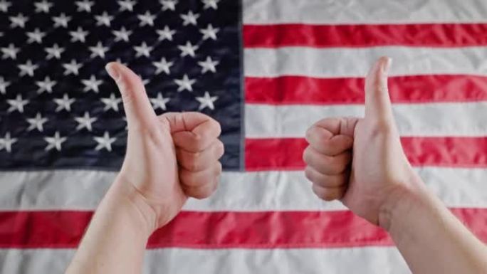 两个白人的手在模糊的美国国旗前竖起大拇指