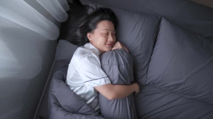 快乐的女人在床上睡觉时微笑着甜蜜的梦拥抱靠垫。顶视图。