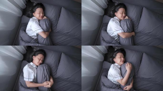 快乐的女人在床上睡觉时微笑着甜蜜的梦拥抱靠垫。顶视图。