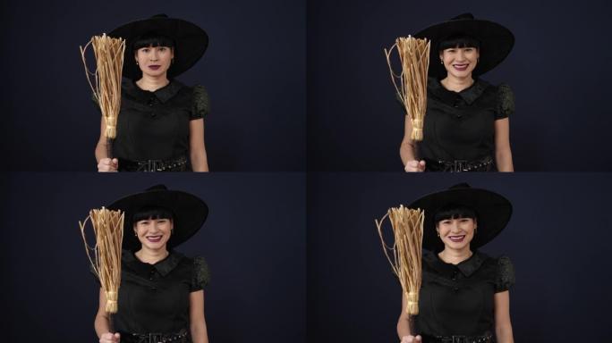 穿着女巫服装的年轻中国妇女在孤立的黑色背景上拿着扫帚
