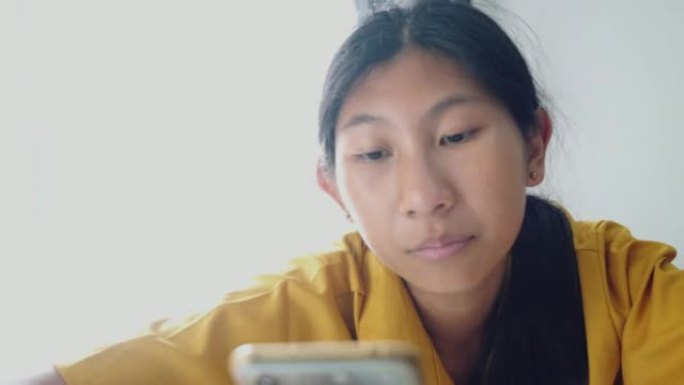 亚洲女孩在家使用靠近窗户的智能手机，生活方式概念。