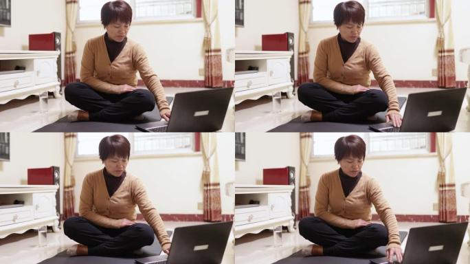 一名中年妇女在瑜伽垫上使用笔记本电脑学习健身方式-技术和生活，健康的生活方式