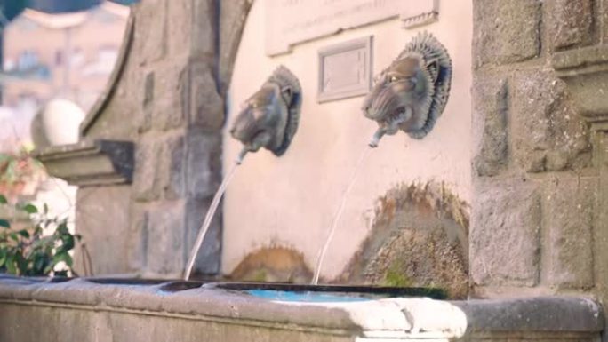 古老的小城市街道上有干净饮用水的建筑喷泉，两个神秘动物形状的青铜水龙头和带有拉丁铭文的大理石板。意大