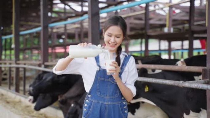 亚洲女奶农在牛棚里拿着一瓶牛奶的肖像。年轻漂亮的女农业农民微笑着看着相机，在畜牧业用幸福挤奶后。