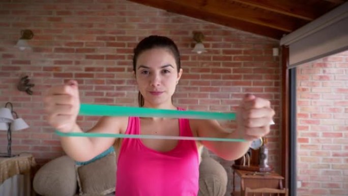 西班牙裔年轻女子在家用阻力带训练手部肌肉。
