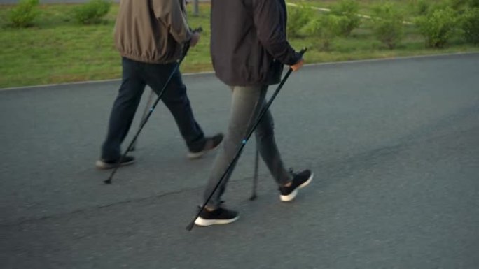 养老金领取者在公园里从事北欧散步。一个男人和一个女人用棍子走路来改善健康。腿靠近。