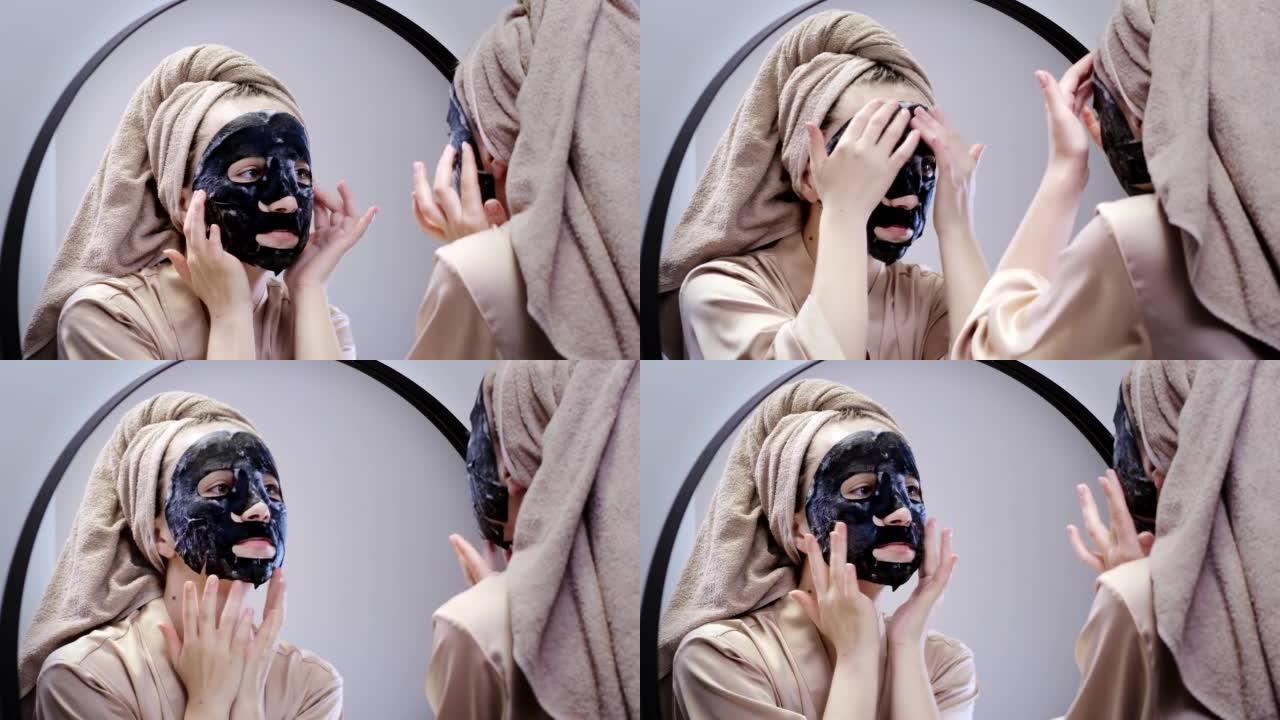 年轻快乐的女人穿着毛巾制作口罩，在时尚的浴室里照镜子。女人用面膜清洁皮肤。护肤。