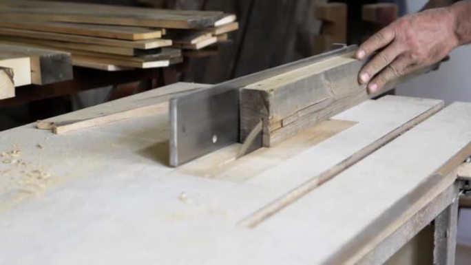 特写: 他车间里的一个木匠用圆锯锯一块木板，在自然光下制作家具零件。木匠在慢动作中使用木材。用于家庭