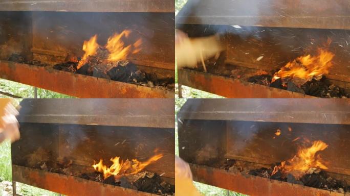 烤肉串人的手在烤肉架上挥舞着一块纸板。烤肉串风扇用平牌在火盆中吹起火焰。慢动作，特写
